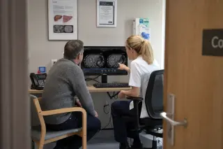 Radiographer and patient sit together in a softly lit imaging room, attentively reviewing liver scan results on a computer, natural daylight creating a calm and supportive ambiance.